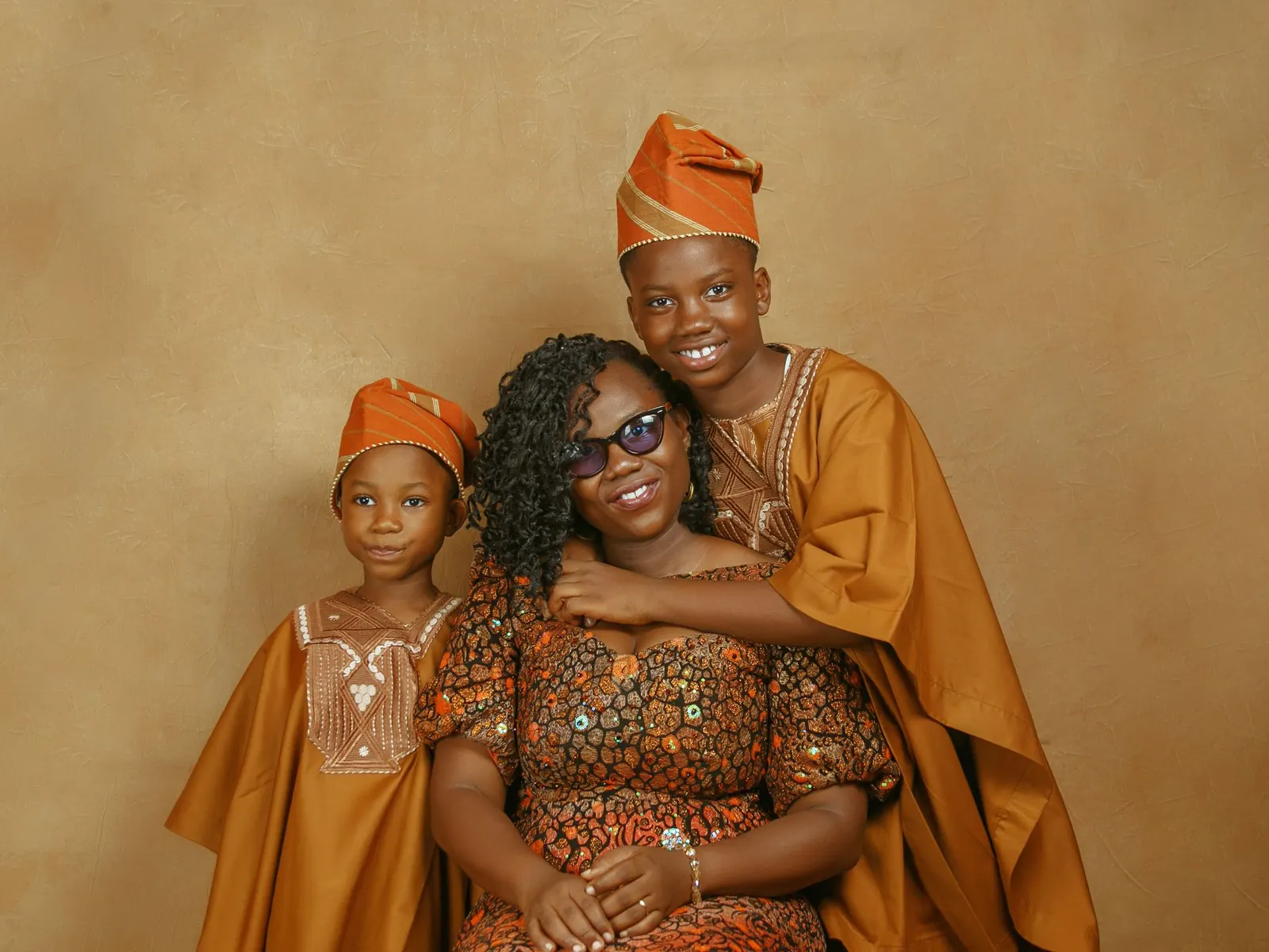 Smiling mother hugging her two children, all in traditional Yoruba outfits